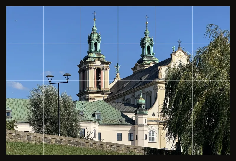 A baroque church with green copper towers beside a willow, divided by a white grid of 6 columns and 4 rows